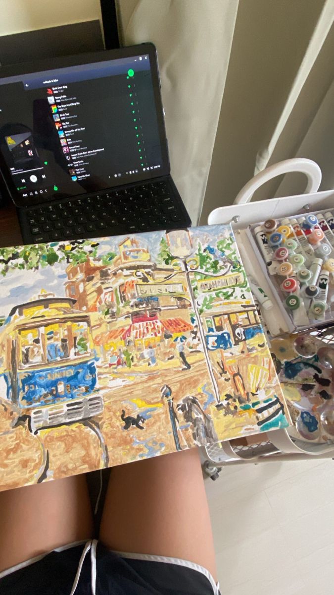 a laptop computer sitting on top of a desk next to a painting with cars and trucks