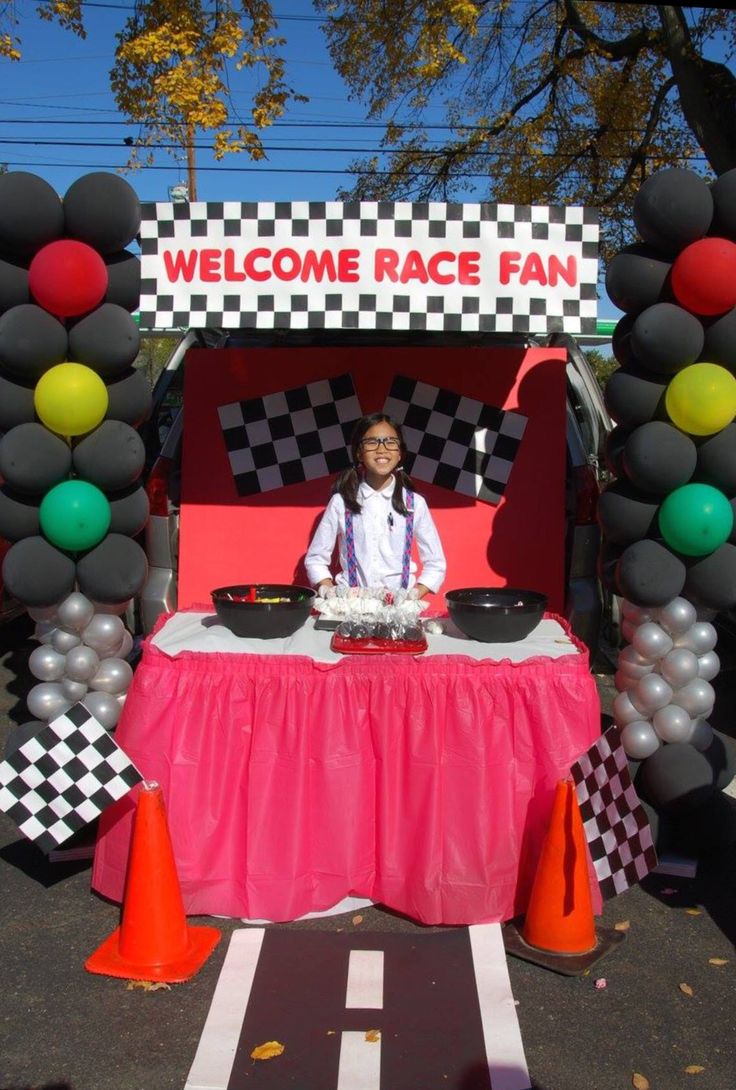 a woman sitting at a table in front of a welcome race fan sign with balloons