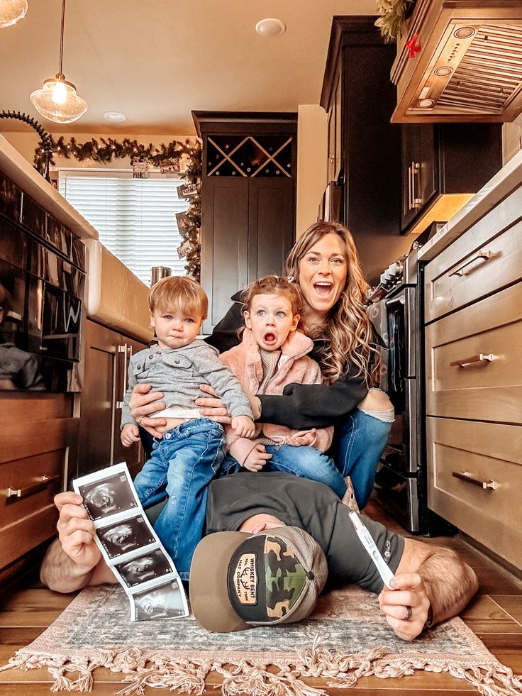 a woman sitting on the floor with two children and an adult holding a baby in her lap