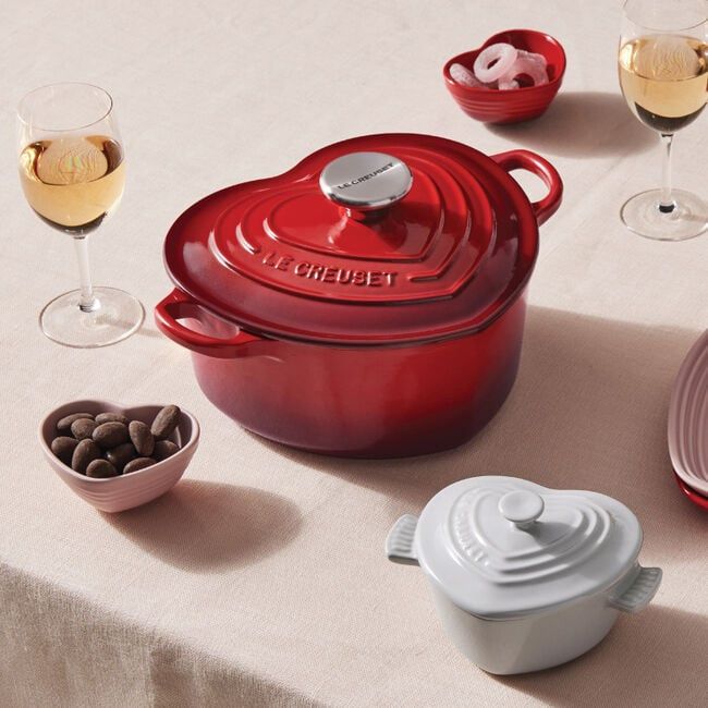 a red casserole dish sitting on top of a table next to wine glasses