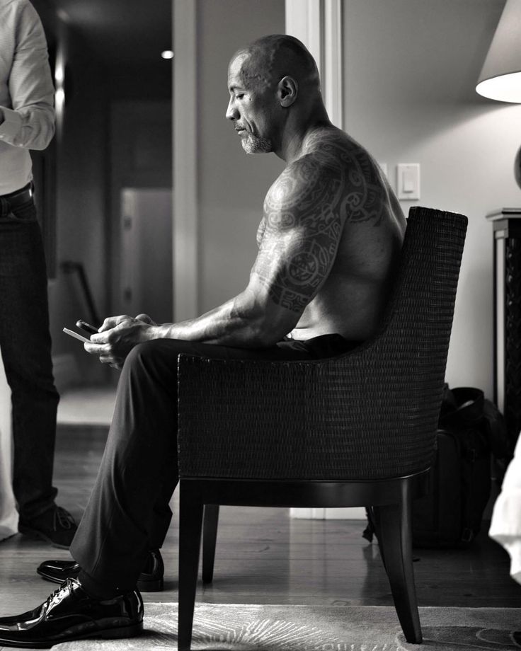 a man sitting in a chair looking at his cell phone while another man stands behind him