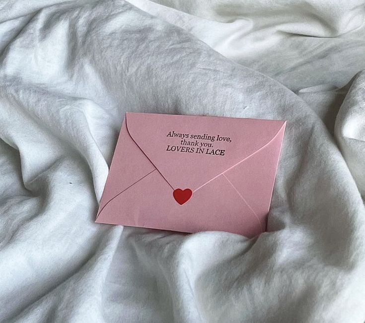 a pink envelope with a red heart on it sitting on a white sheet that says, always sending love to someone else loves in peace