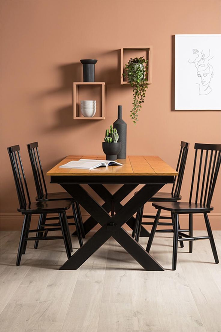 a dining table with four chairs and a vase on the wall in front of it