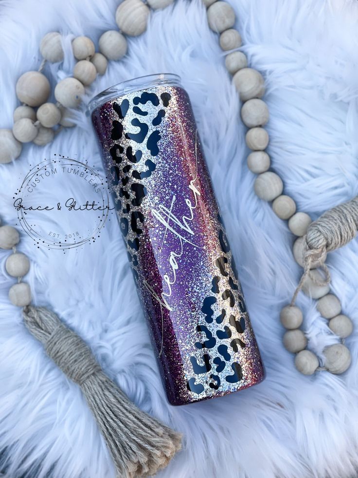 a purple and black leopard print tumbler with tassels next to it on a white fur rug