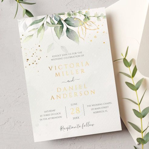 an elegant wedding card with greenery and gold foil on the front is displayed next to a white envelope