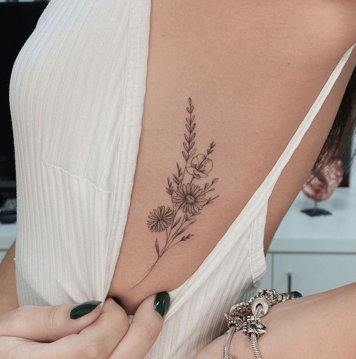 a woman with a flower tattoo on her upper arm and lower back, holding onto the shoulder