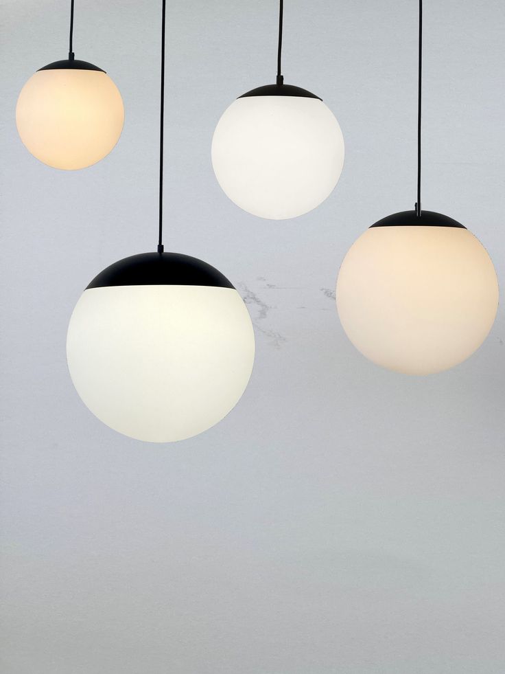 three white and one black globe lights hanging from the ceiling in front of a gray background