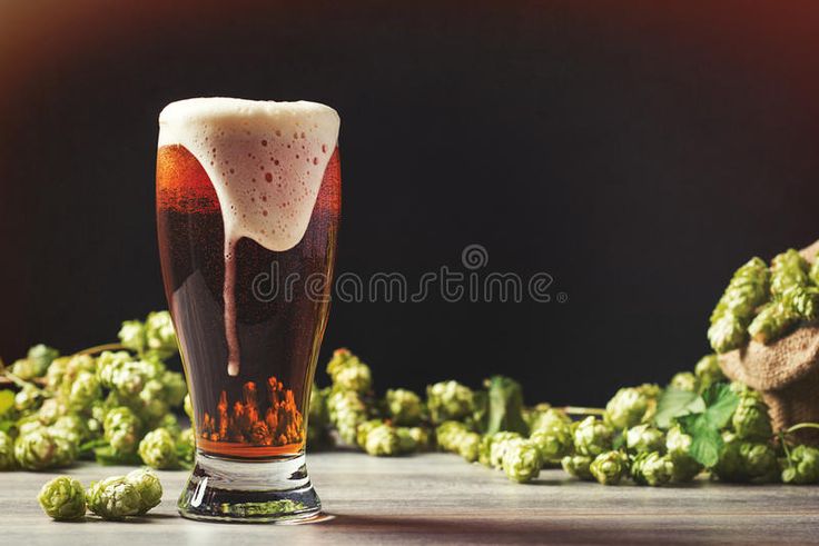 a tall glass filled with beer next to hops