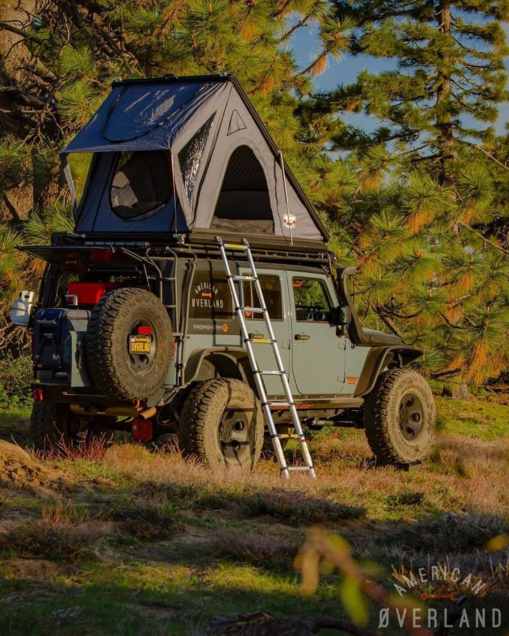 an off - road vehicle with a tent on the roof is parked in front of some trees