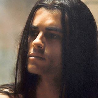 a close up of a person with long hair and no shirt on holding a cell phone