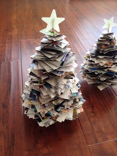 two small christmas trees made out of newspapers on a wooden floor with white candles in them