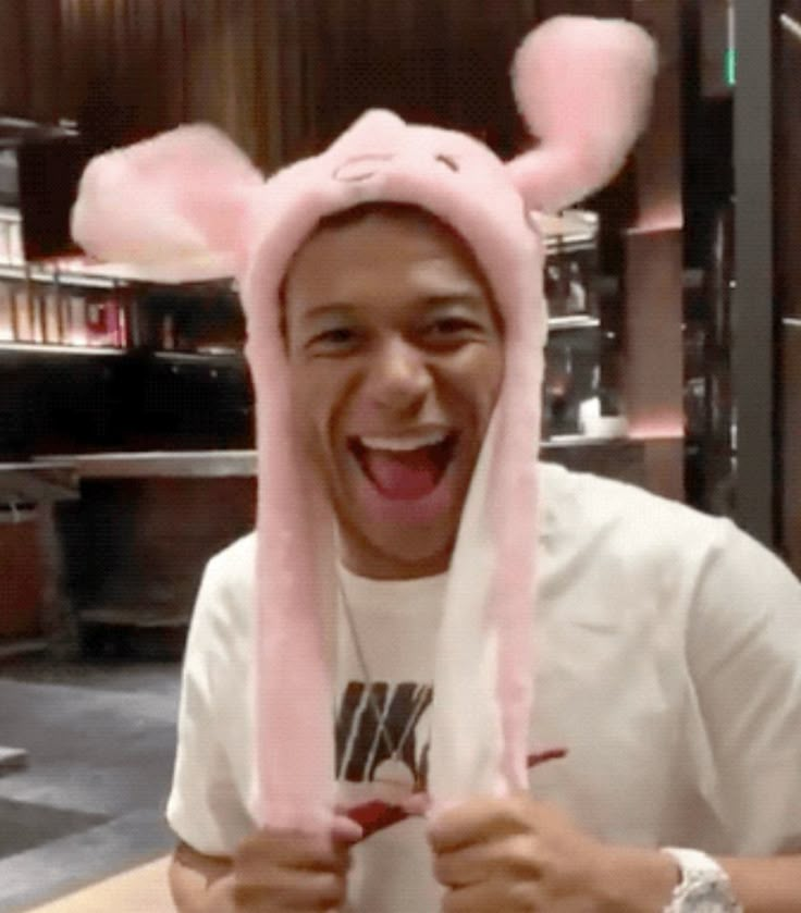 a man with bunny ears on his head is smiling and holding up a pink hat