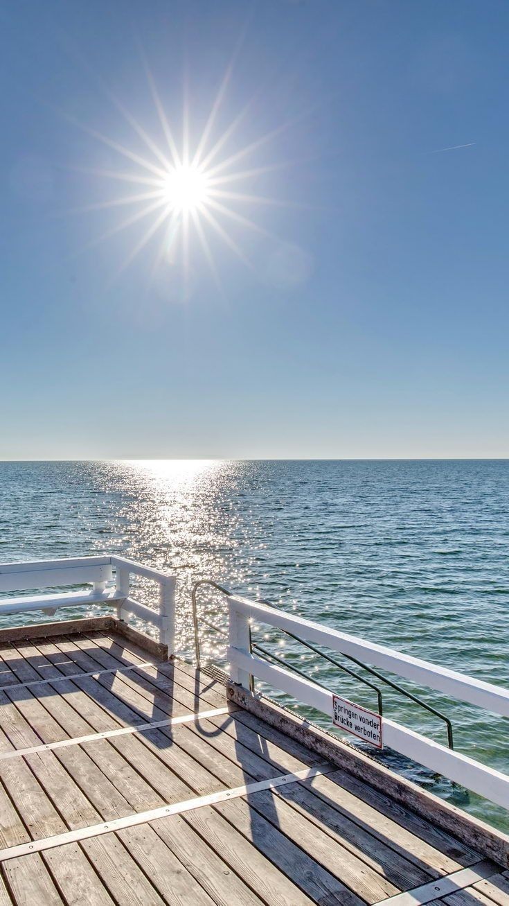 the sun shines brightly over the ocean as it sits on a pier next to the water