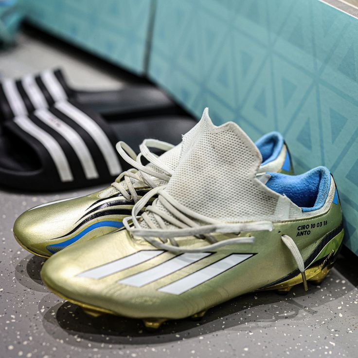 two soccer shoes sitting next to each other on the ground in front of a wall