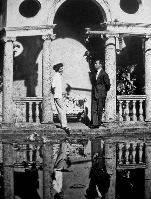 two men standing on the balcony of an old building with water in front of them