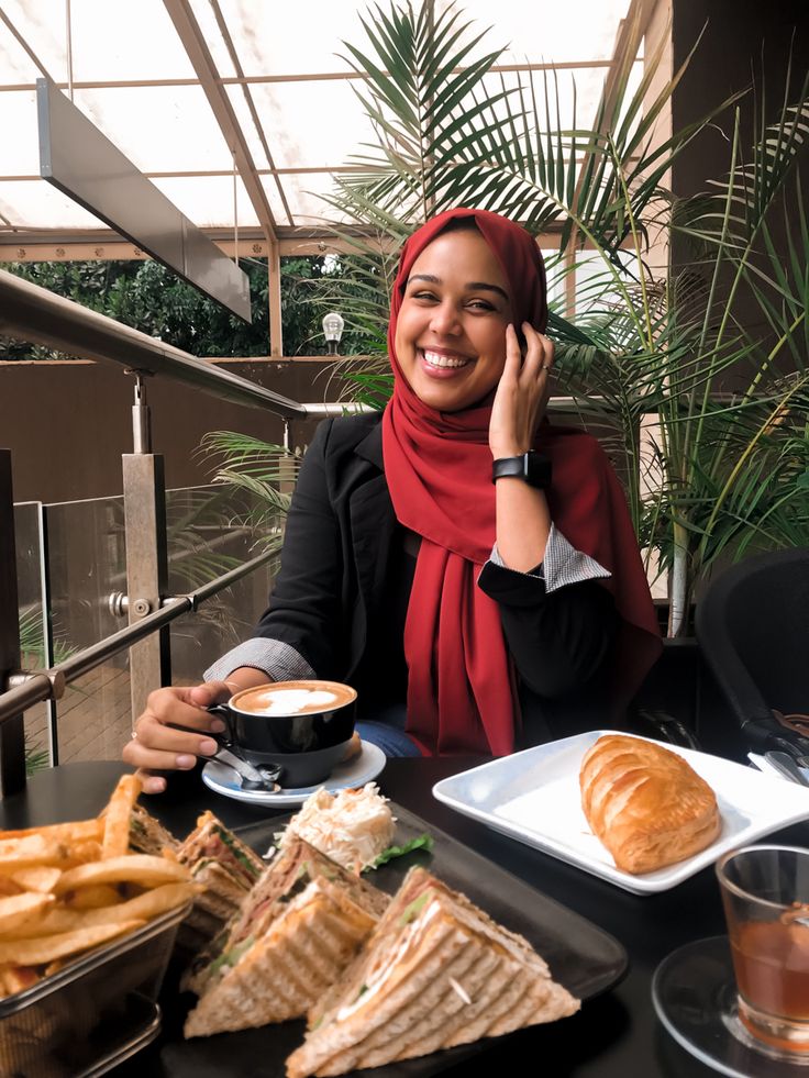 a woman sitting at a table with food and drinks in front of her, talking on the phone