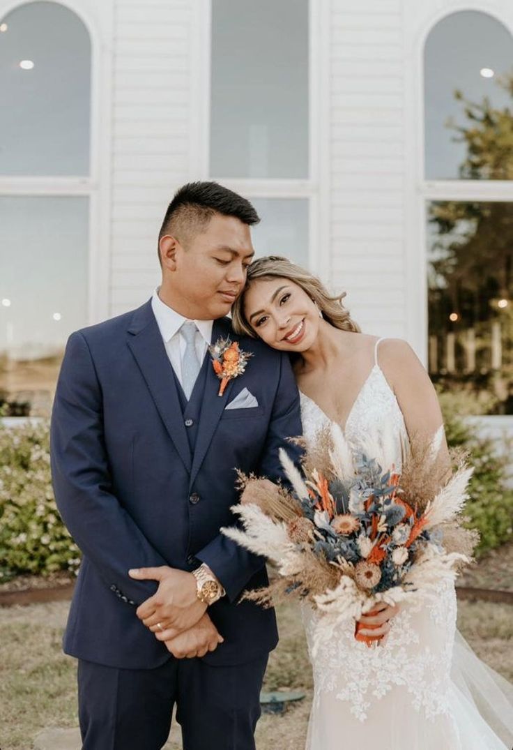 a bride and groom standing in front of a white church with their arms around each other