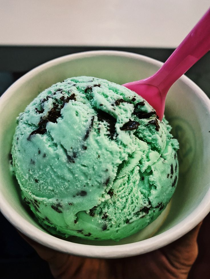 a hand holding a bowl filled with green ice cream