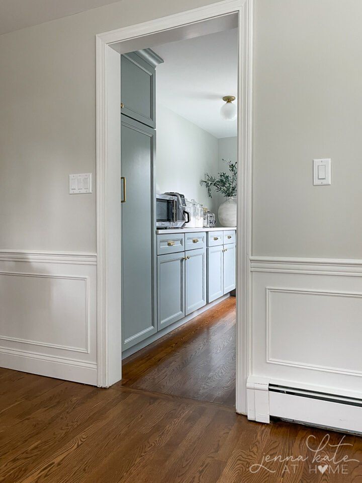 an open door leading to a kitchen with white walls and wood flooring on the other side