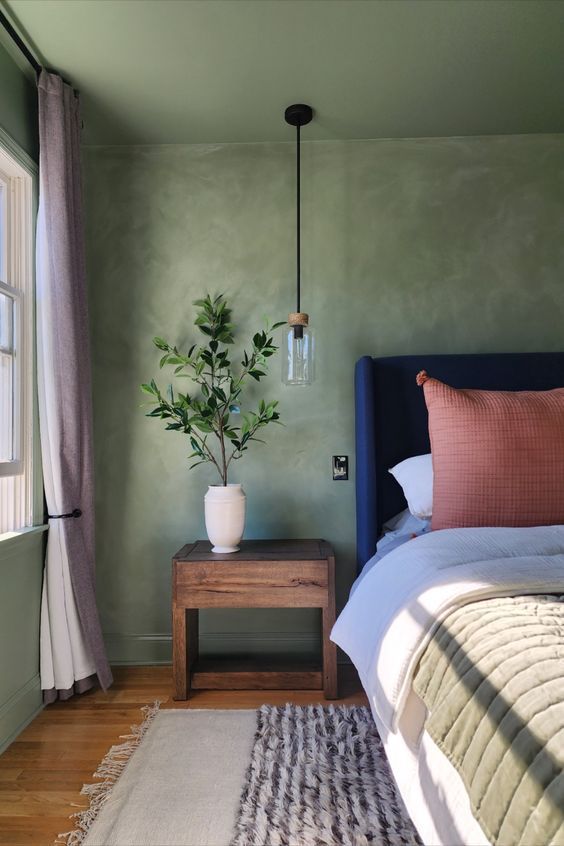 a bed sitting next to a window with a plant on top of the headboard