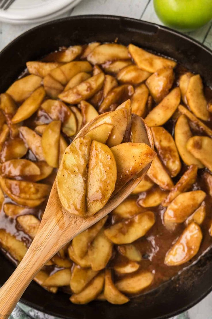 a wooden spoon in a skillet filled with apple slices and caramel glaze