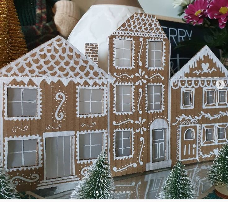 three gingerbread houses are on display in front of some christmas trees and other decorations