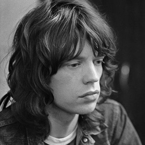 a black and white photo of a young man with long hair wearing a denim jacket