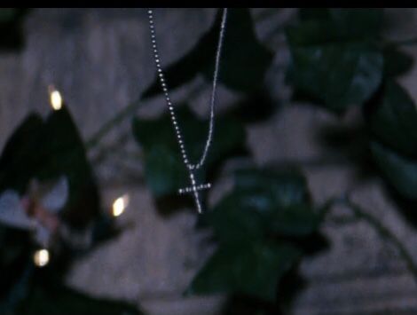 a necklace with a cross hanging from it's side on a table next to some leaves