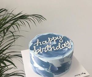 a blue and white birthday cake sitting on top of a table next to a potted plant