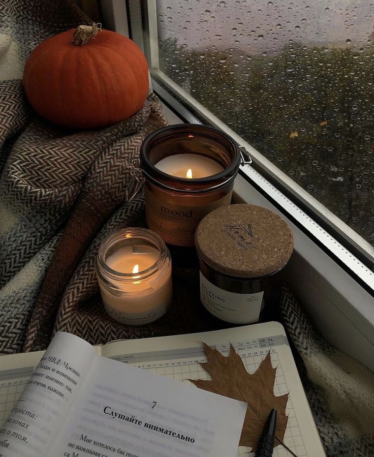 an open book sitting on top of a window sill next to candles and a pumpkin