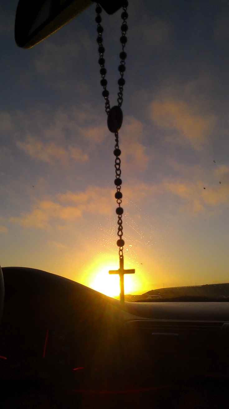 the sun is setting behind a car with a rosary hanging from it's dashboard