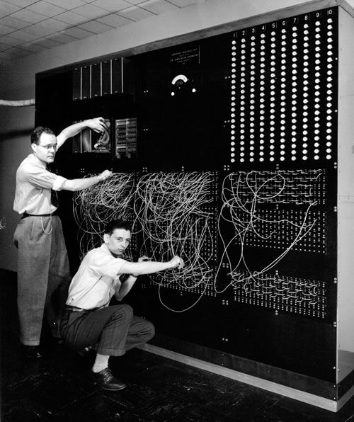 two men working on an electrical panel with wires attached to the wall and in front of them