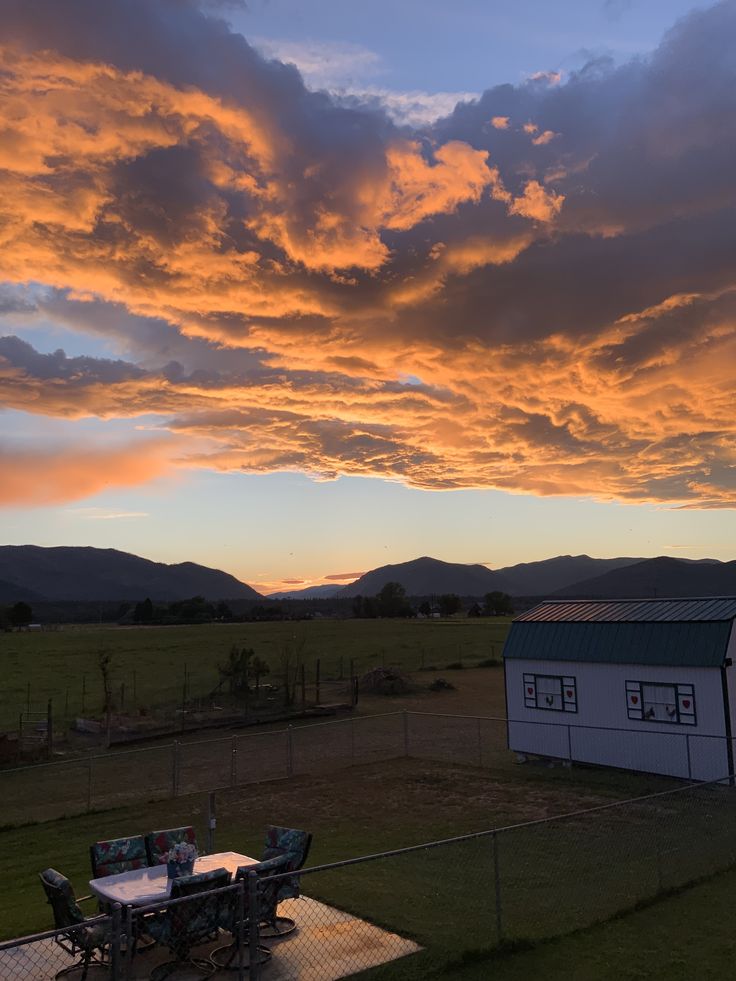 the sun sets over a farm house with a table and chairs in the foreground