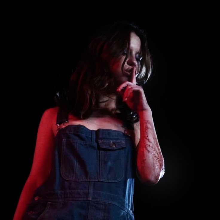 a woman in overalls holding a microphone up to her mouth with blood all over her body