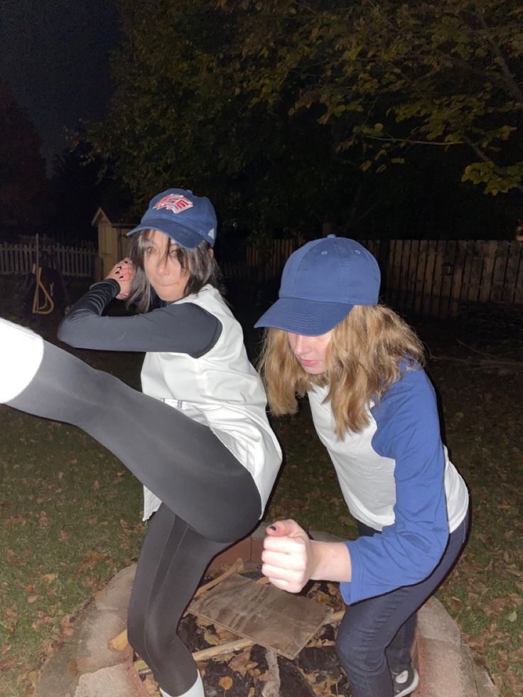 two young women are playing baseball outside at night