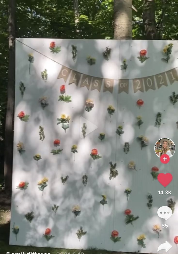 a sign with flowers on it in the woods next to a tree and two people's faces