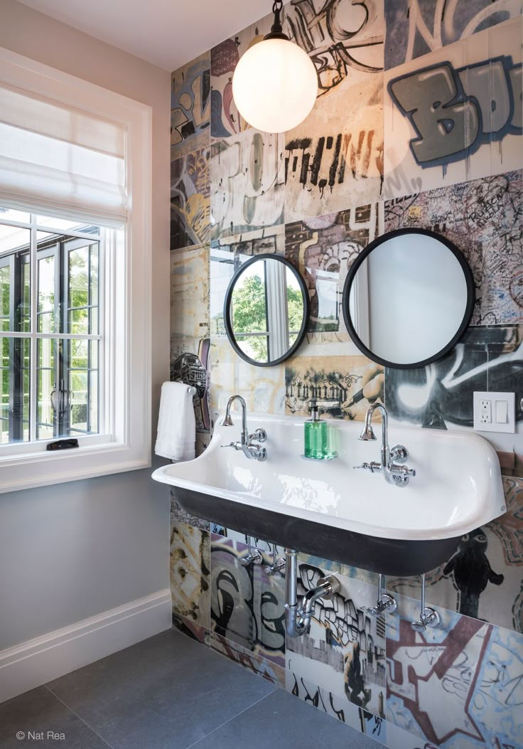 a bathroom with graffiti on the wall and two round mirrors hanging from the ceiling above the sink