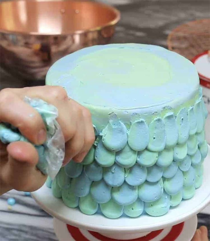 someone is decorating a cake with blue icing on the top and green frosting on the bottom