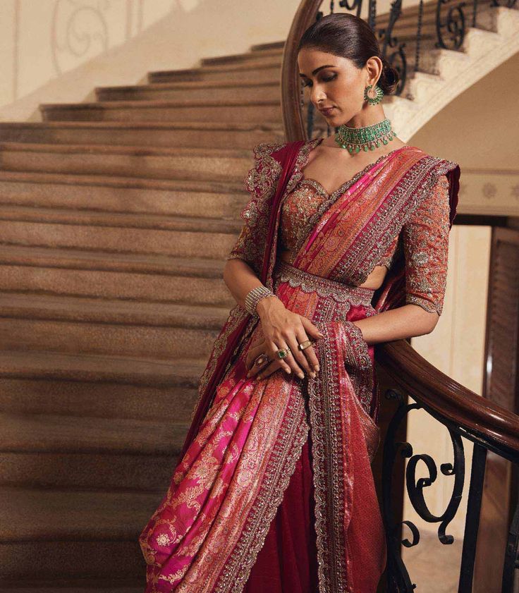 a woman in a red and gold sari standing next to some stairs with her hands on her hips