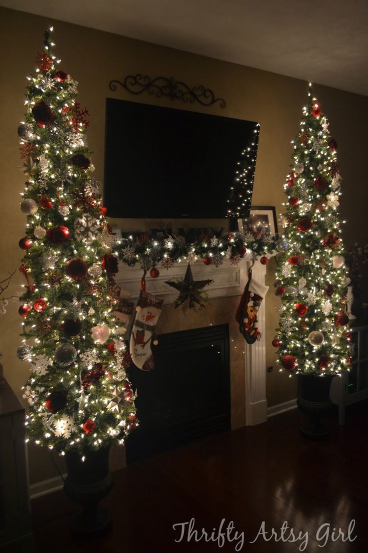 two decorated christmas trees in front of a fireplace