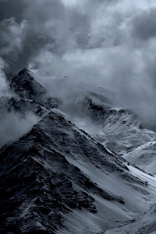 black and white photo of snow covered mountains under cloudy skies, with dark clouds in the background