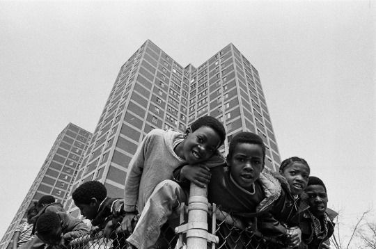 black and white photograph of children playing in front of tall buildings with skyscrapers behind them