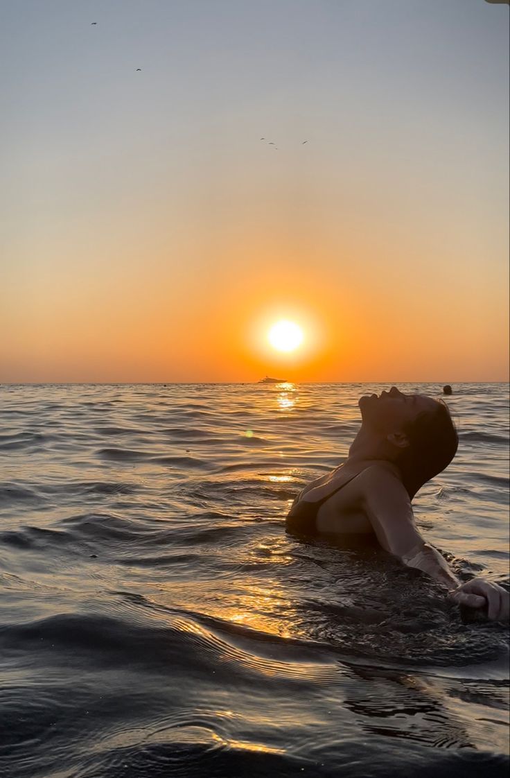 a person floating in the ocean at sunset with their back turned to the camera,