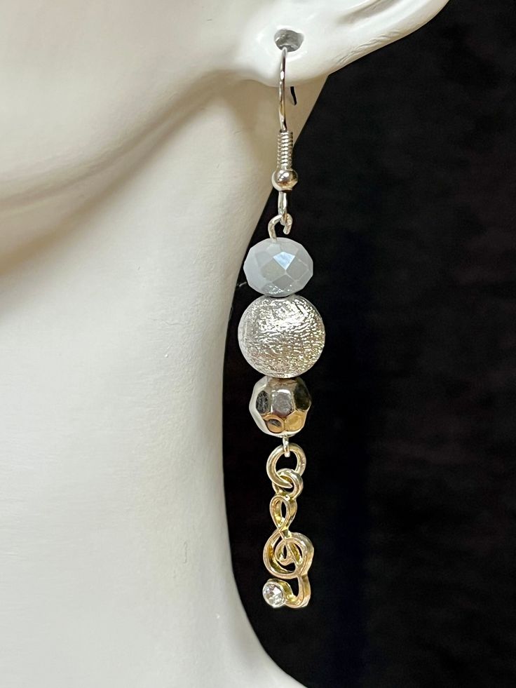 An earring for the music lover in all of us with a touch of style added. The gray glass bead starts this earring. Then a little larger silver sparkle bead. Finally, a smaller, textured silver bead with a silver treble clef charm. Silver Nickel-free Music-themed Earrings, Music-themed Silver Earrings, Silver Beaded Metal Earrings As Gift, Silver Metal Beaded Earrings For Gift, Silver Single Beaded Earring For Party, Silver Party Earrings With Faceted Beads, Silver Round Bead Earrings For Party, Silver Round Beads Earrings For Party, Silver Earrings With Round Beads For Party