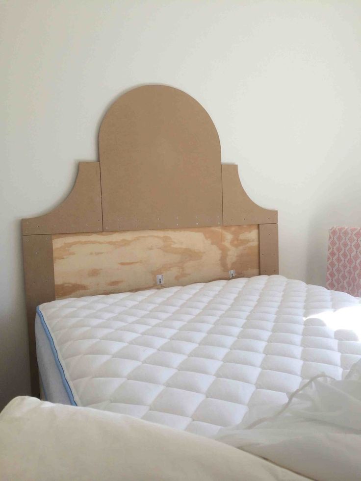 a bed with a wooden headboard and white sheets on it's side, next to a pink lamp