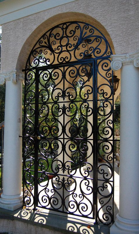 an iron gate is open on the side of a building with columns and arches in front of it