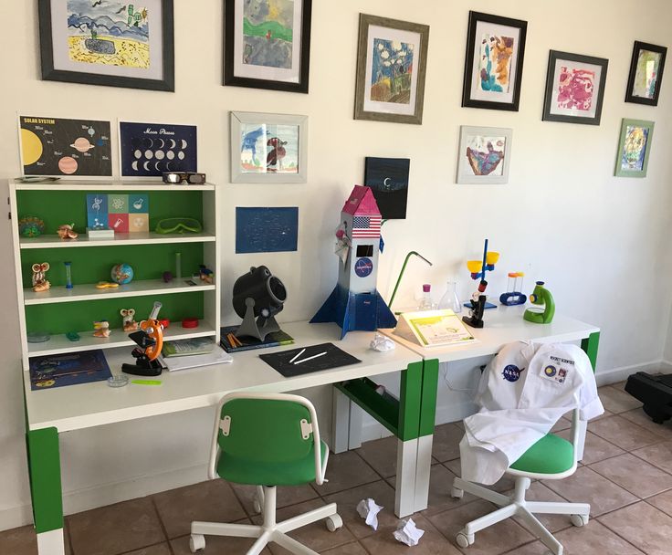 a green and white desk in a room with pictures on the wall above it, along with two children's chairs