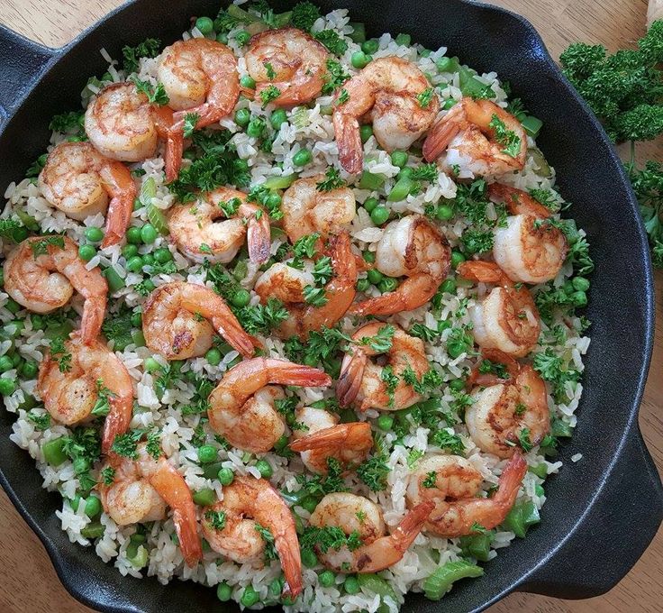 a skillet filled with rice and shrimp on top of a wooden table