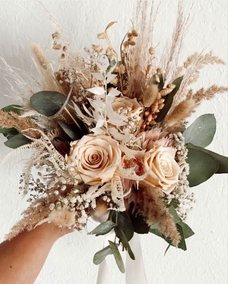 a person holding a bouquet of flowers in their hand with white and brown foliage on it