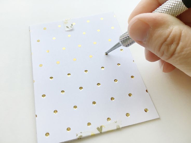 a person is holding a pen and writing on a piece of paper with gold dots